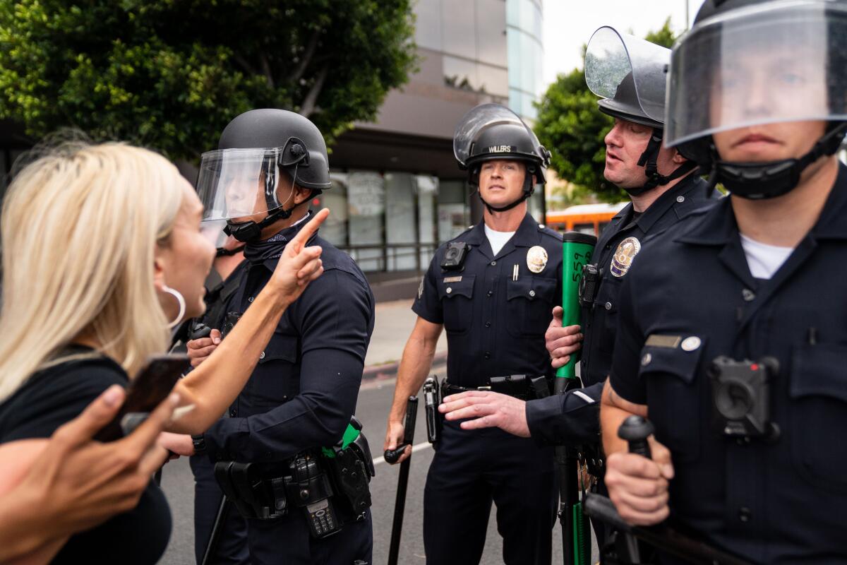A woman points her finger toward police officers wearing helmets