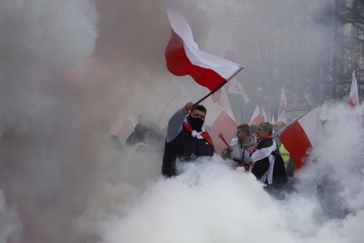 A man cloaked in smoke waves a Polish flag