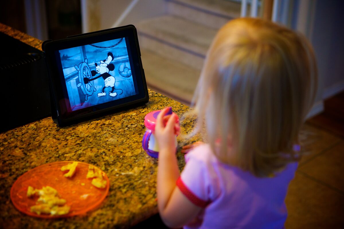 A young child watches a Mickey Mouse cartoon featuring Steamboat Willie. 