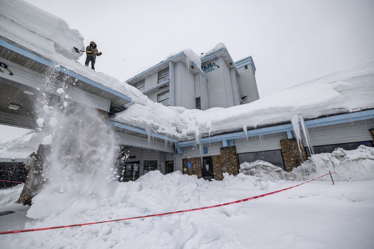 A worker shovels snow from a roof at the Shilo Inn in the first days of spring on March 21, 2023 in Mammoth Lakes, Calif. 