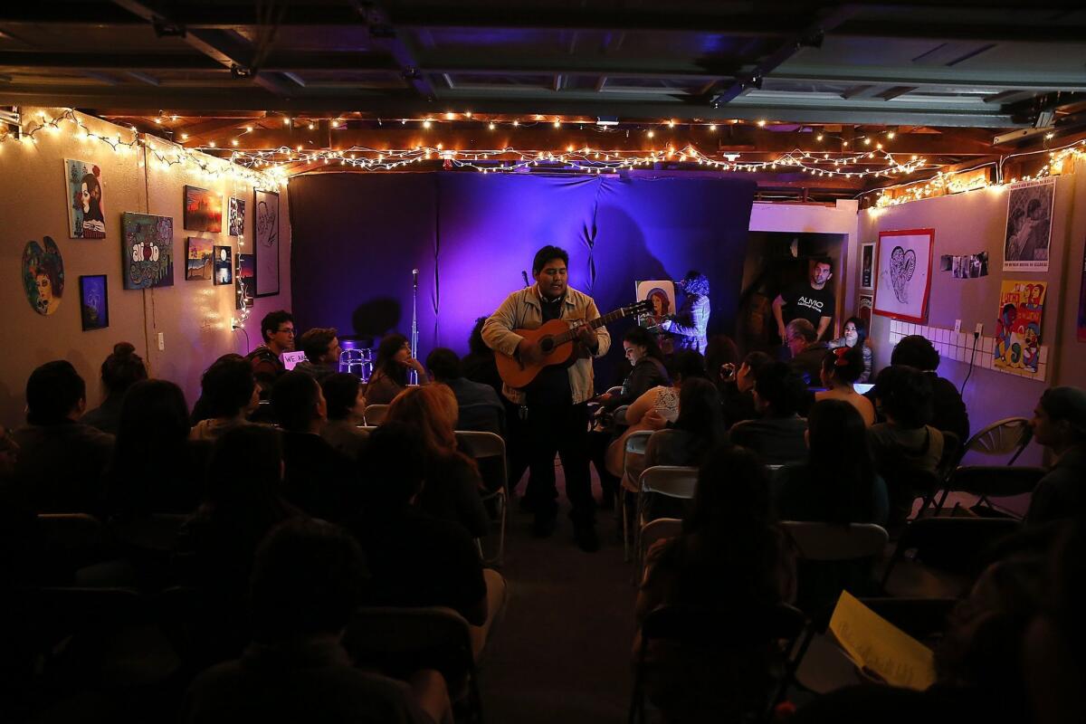 Dozens of people crowd the driveway and garage as Julio Marquez performs folk songs during the Alivio open mic night at the garage of Eric Contreras in Bell.