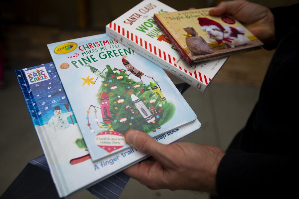 Matt Mayo holds a selection of Christmas-themed kids' books at Once Upon a Time bookstore.