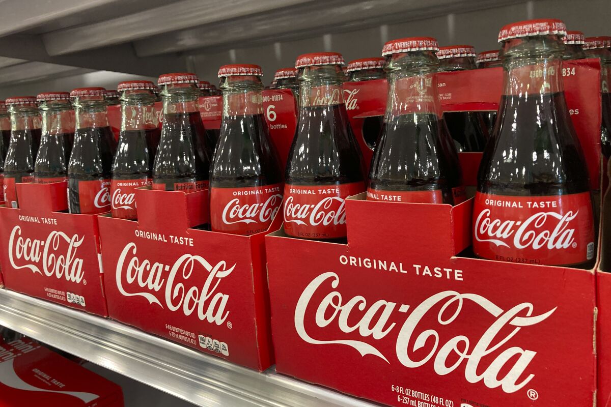 Bottles of Coca-Cola are stacked on a shelf in a grocery store, Wednesday, Dec. 15, 2021, in Surfside, Fla. Coca-Cola’s revenue rose 10% to $9.5 billion in the fourth quarter, Thursday, Feb. 10, 2022, as coffee shops, movie theaters and other venues continued to reopen. The Atlanta-based beverage giant said the fourth quarter was the first time since the pandemic that away-from-home sales volumes were ahead of 2019 levels.(AP Photo/Wilfredo Lee)