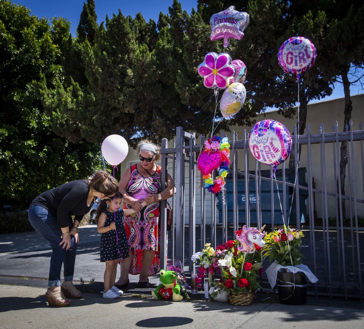 Veronica Fregoso, left, her daughter Bella, 3, and her mother, Esther Fregoso pause in front of a small memorial after placing flowers and a rosary at the site where 8-month-old Alexia Rose Echeverria was found dead.