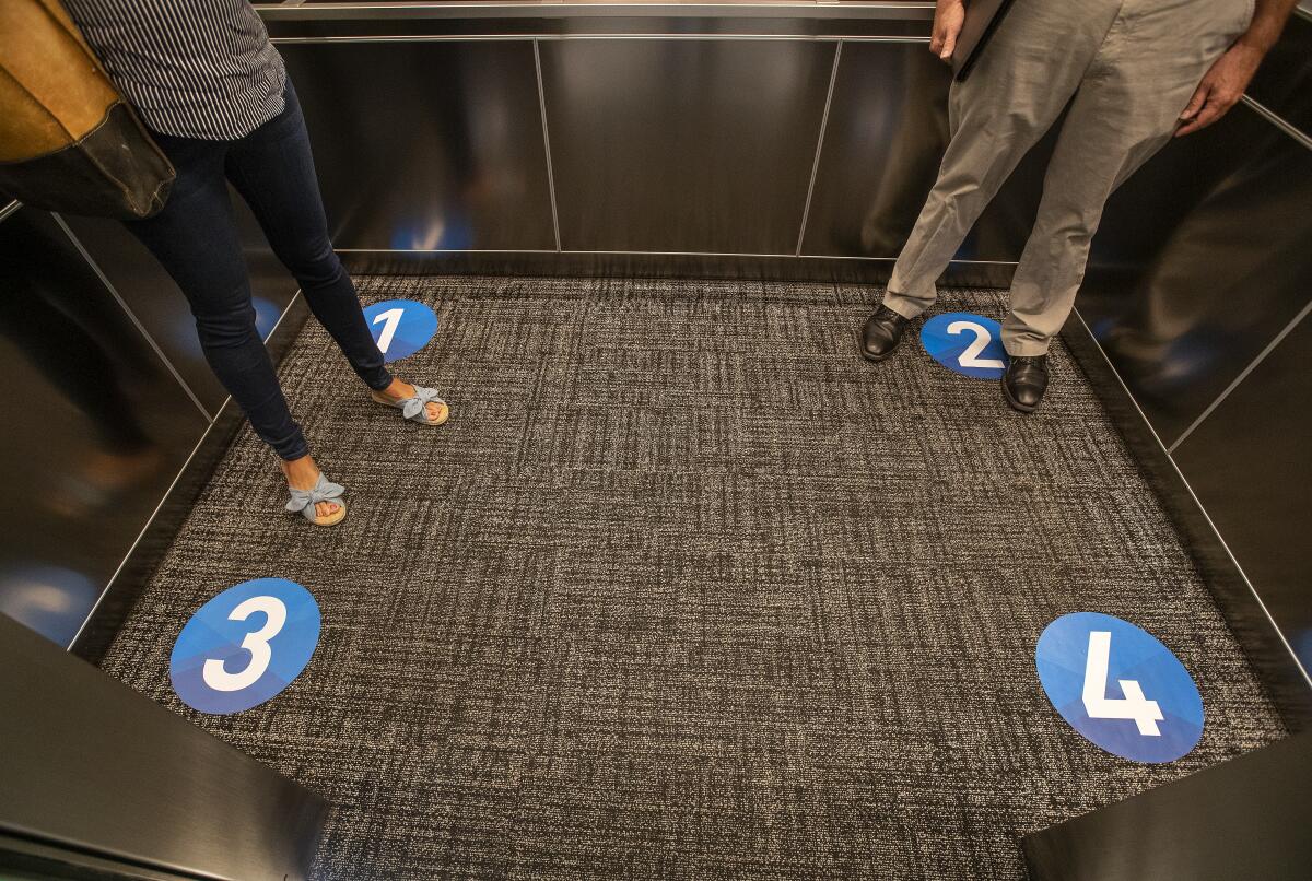 Two people stand inside an elevator with social-distancing decals on the floor