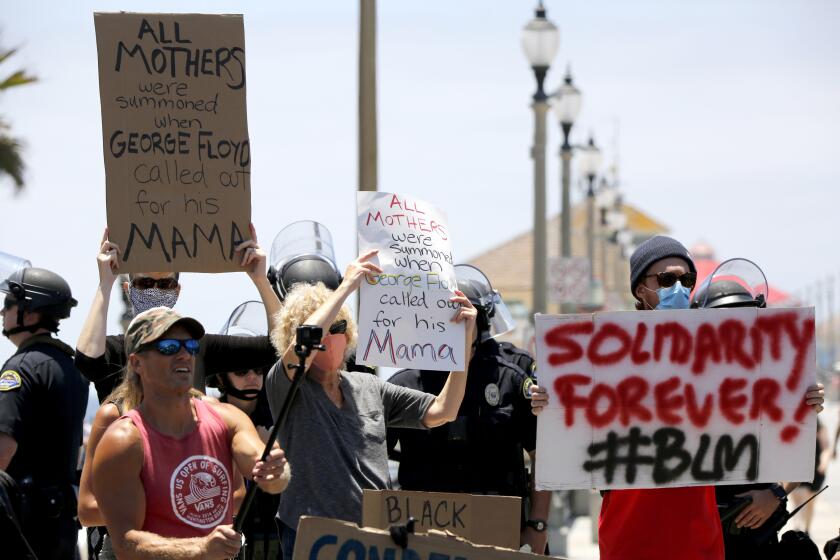 Protesters hold up signs during Saturday's protest in in Huntington Beach.