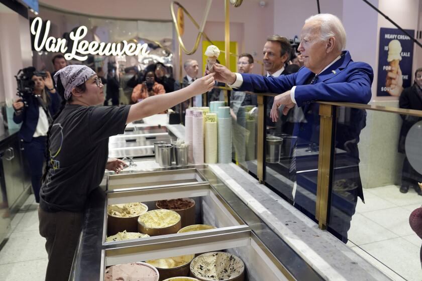 El presidente Joe Biden recibe un helado en la heladería Van Leeuwen Ice Cream, el lunes 26 de febrero de 2024, en Nueva York. Detrás de él se encuentra el presentador televisivo Seth Meyers. (AP Foto/Evan Vucci)