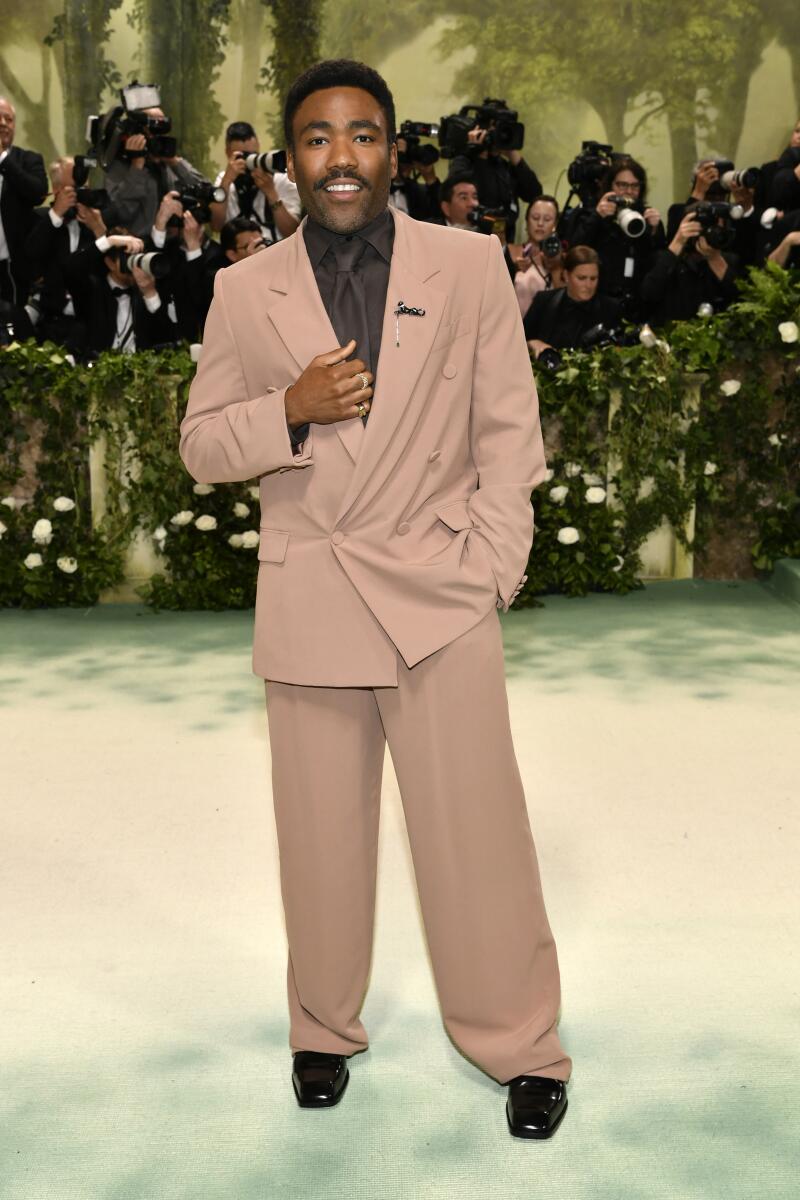 Donald Glover shows how the colors of rich earth — peat moss brown and tan clay — work in a fluid, double-breasted ‘90s style suit with wide trouser legs and the era’s wide tie, all by Saint Laurent’s Anthony Vaccarello.