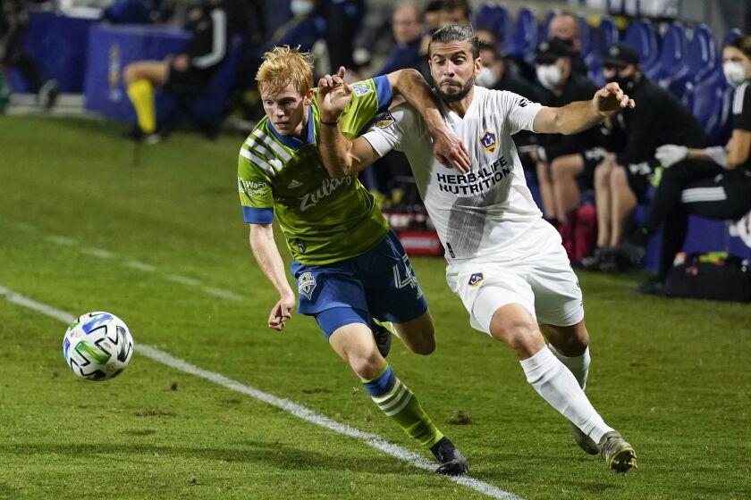 Seattle Sounders midfielder Ethan Dobbelaere, left, and LA Galaxy defender Emiliano Insua keep the ball in play during the first half of an MLS soccer match Wednesday, Nov. 4, 2020, in Carson, Calif. (AP Photo/Ashley Landis)