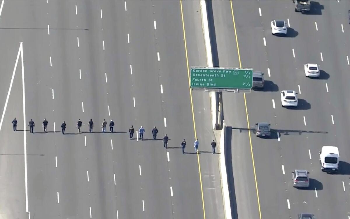 A line of people walk along empty freeway lanes.