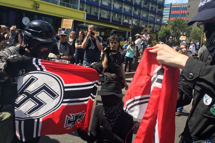 Counter protesters tear a Nazi flag, Saturday, Aug. 4, 2018 in Portland, Ore. Small scuffles broke out Saturday as police in Portland, Oregon, deployed "flash bang" devices and other means to disperse hundreds of right-wing and self-described anti-fascist protesters. (AP Photo/Manuel Valdes)