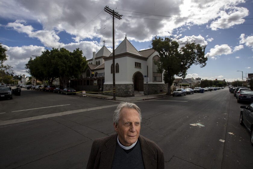 Father Thomas Carey stands on a street corner with the Church of the Epiphany in the background. 