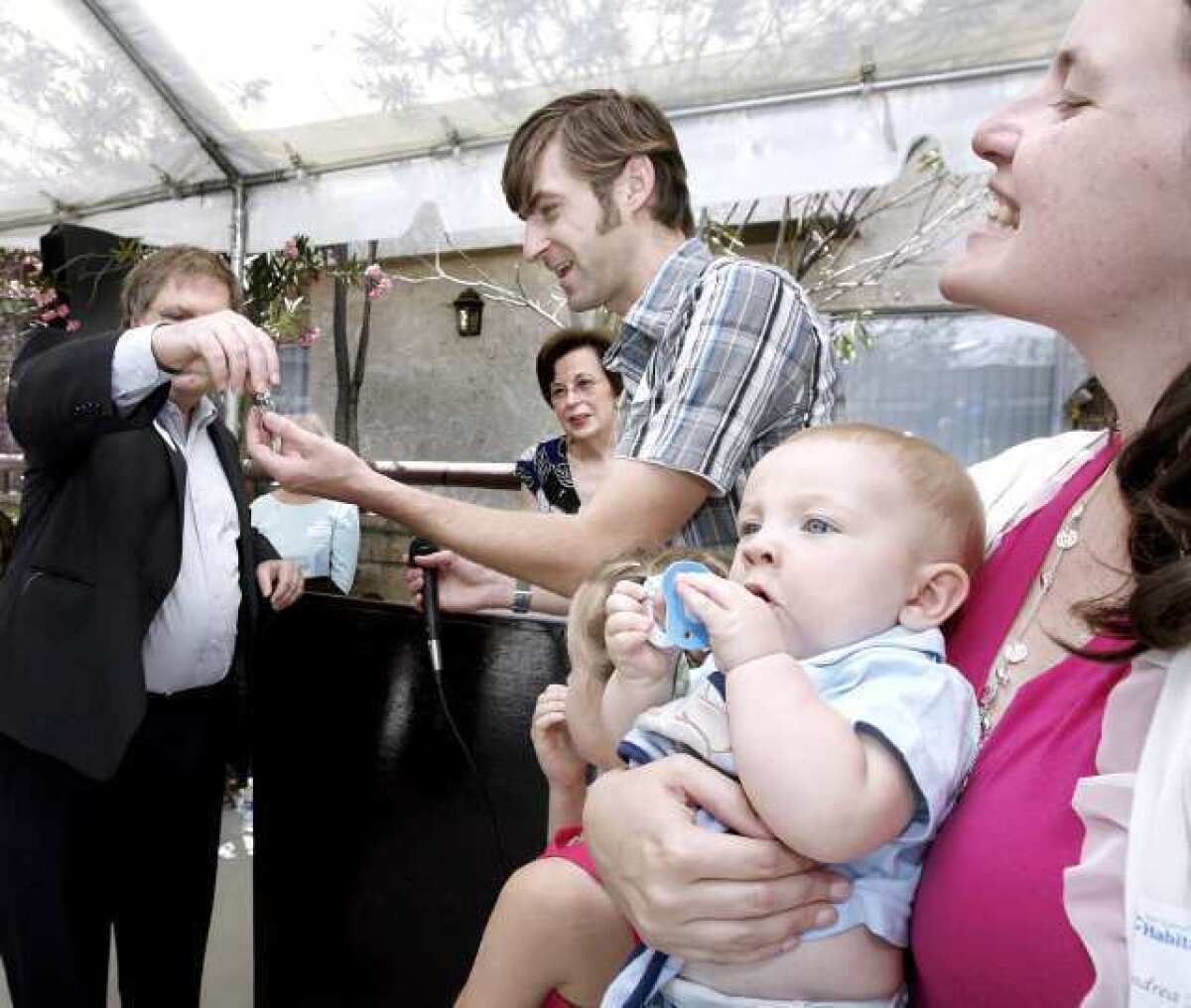 San Gabriel Valley Habitat for Humanity board member Thomas Bunn III, left, hands the keys to their new home to Shane Mulholland as his wife Andrea and baby Luke look on during ceremony for the Geneva Street homes in Glendale.