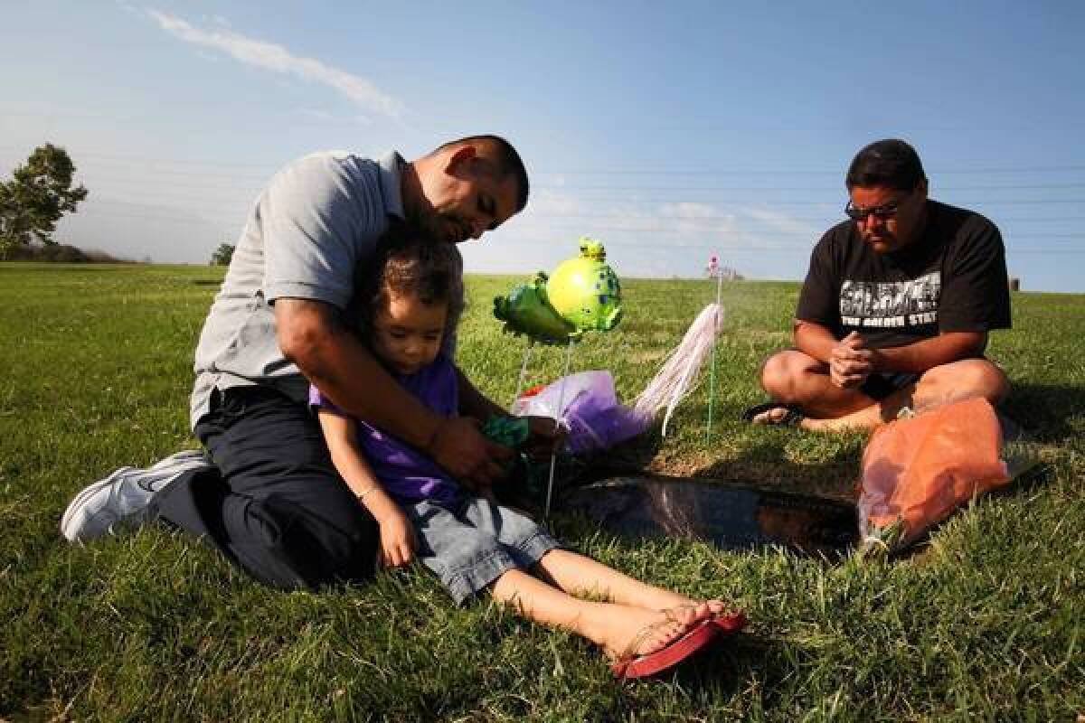 Jose Vasquez holds daughter Angie, 3, as he sits with brother Raymond Vasquez at the grave of their sister Tayde Vasquez at Rose Hills Memorial Park in Whittier. Tayde was shot to death 20 years ago, when she was 13 years old.