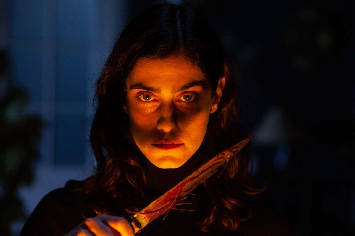 A woman in firelight holds a knife in front of her face.