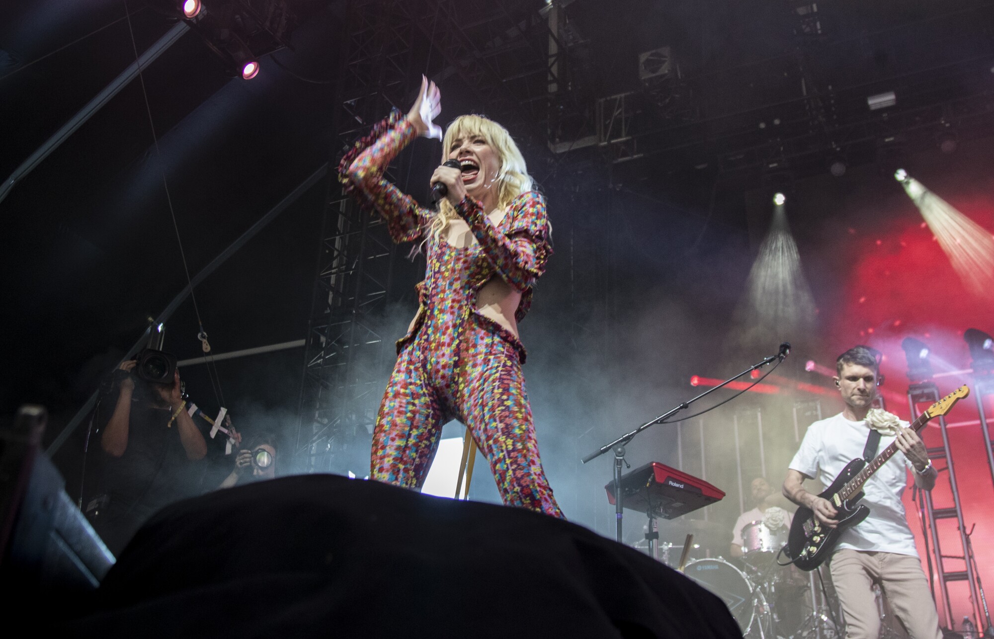 Carly Rae Jepsen in a multicolored outfit performs with bandmates on stage.