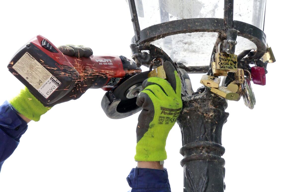 A Paris city employee uses a grinder to cut locks from a street lamp on the Pont des Arts in Paris.