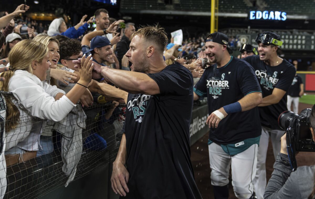 Seattle Mariners, including Jarred Kelenic, foreground, Cal Raleigh, second from left, and another player celebrate with fans after the team's baseball game against the Oakland Athletics, Friday, Sept. 30, 2022, in Seattle. The Mariners won 2-1 to clinch a spot in the playoffs. (AP Photo/Stephen Brashear)