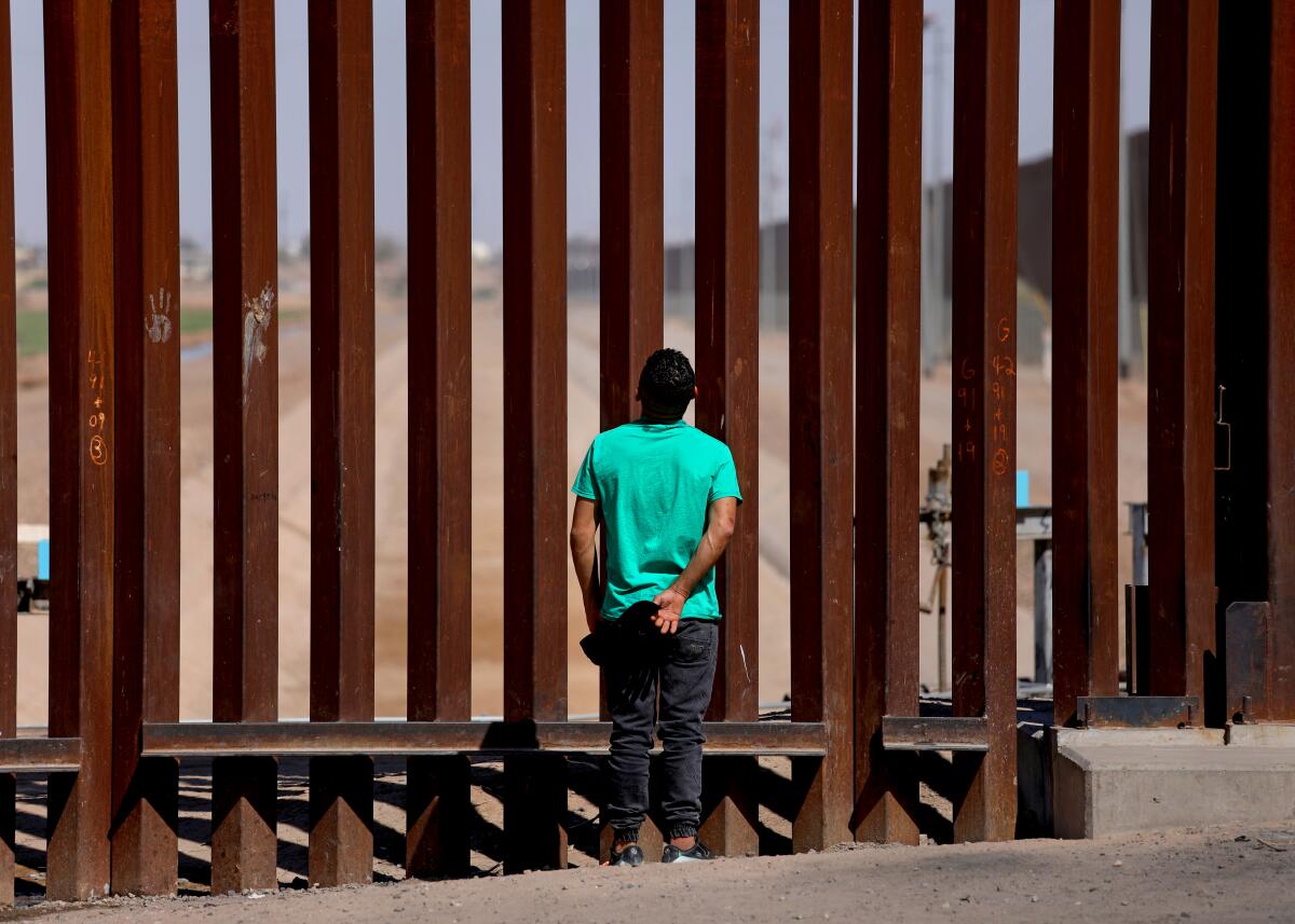 A migrant looks at the border wall while waiting to turn himself over to U.S Border Patrol agents.