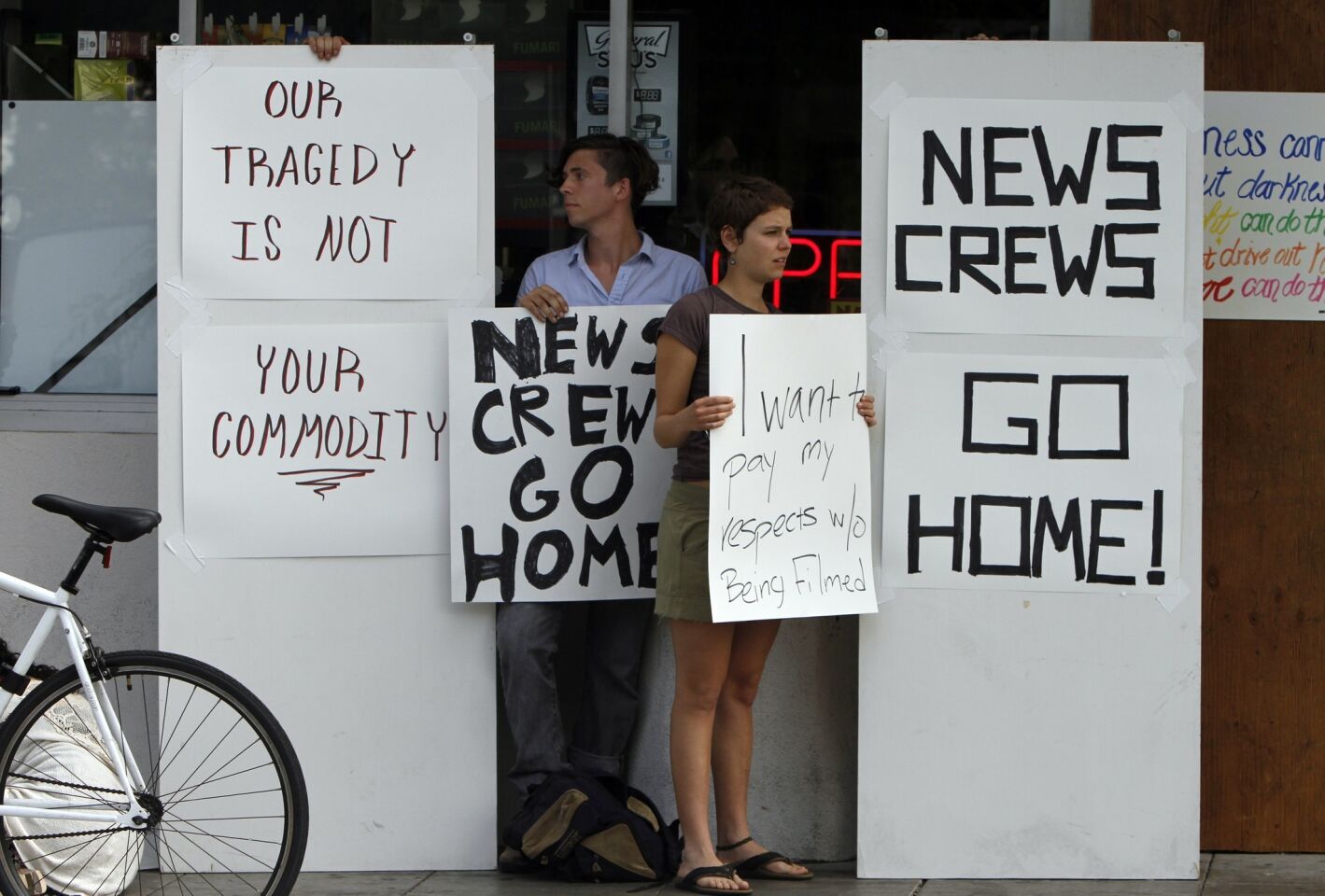 People stand with signs reading "News Crew Go Home" in front of the I.V. Deli Mart in Isla Vista.