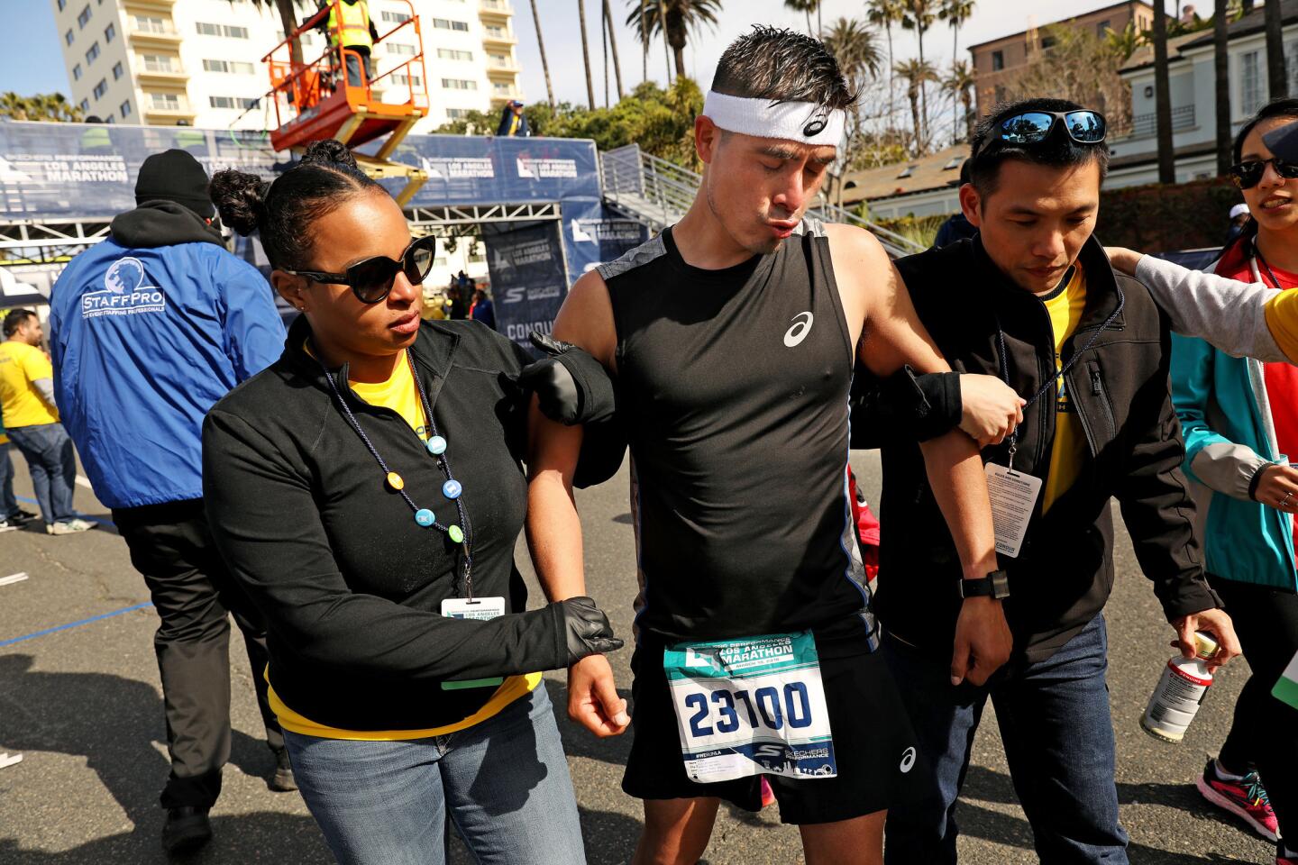 Race participant Jose Bustamante, center, is assisted by volunteers after finishing the L.A. Marathon on Sunday.