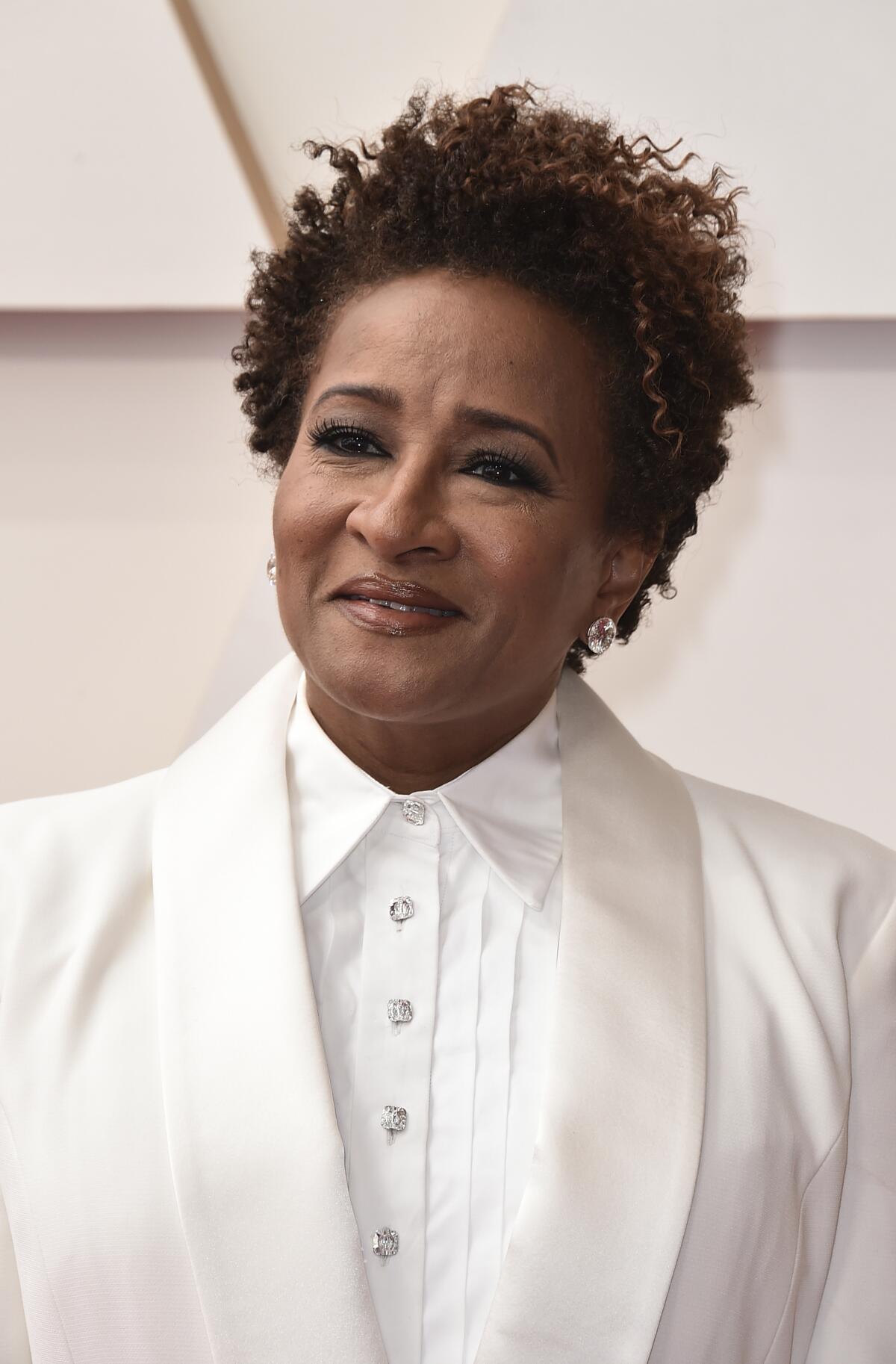 A Black woman wearing a white tuxedo poses on a red carpet