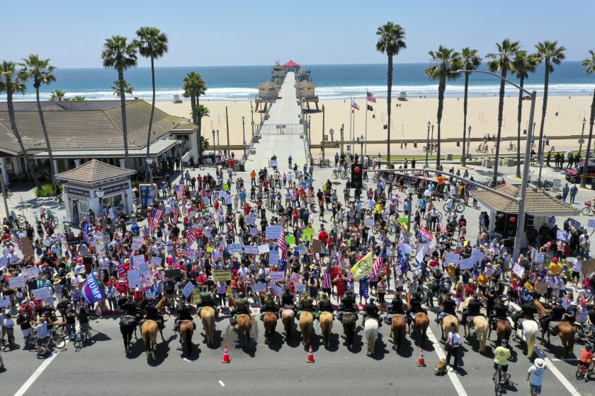 HUNTINGTON BEACH, CA -- FRIDAY, MAY 1, 2020: Thousands of protesters rally at the intersection of Main Street and Pacific Coast Highway in the``March to Open California'' to call on Gov. Newsom to relax the state's stay-at-home orders under COVID-19 in Huntington Beach, CA, on May 1, 2020. Mounted police line up to keep protesters on the sidewalk. (Allen J. Schaben / Los Angeles Times)