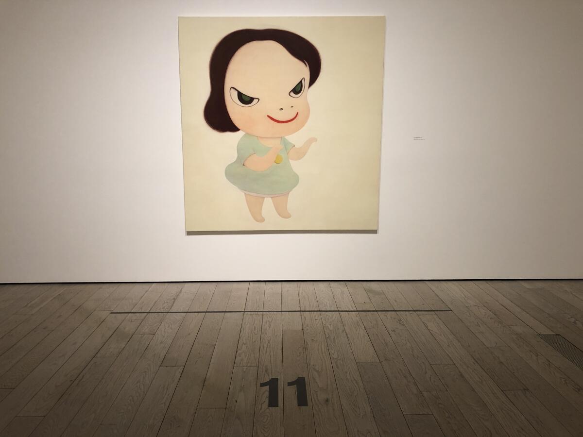 A painting featuring a little girl with a devilish grin. Before it is a large "11" on the gallery floor.