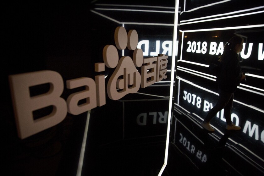 FILE - In this Nov. 1, 2018, file photo, an attendee walks past a display at the 2018 Baidu World conference in Beijing. China’s market regulator said Friday, March 12, 2021, that it fined 12 companies, including games company Tencent Holdings and Chinese search engine firm Baidu Inc., for not disclosing past deals as authorities step up scrutiny over anti-monopoly behavior in the internet sector. (AP Photo/Mark Schiefelbein, File)