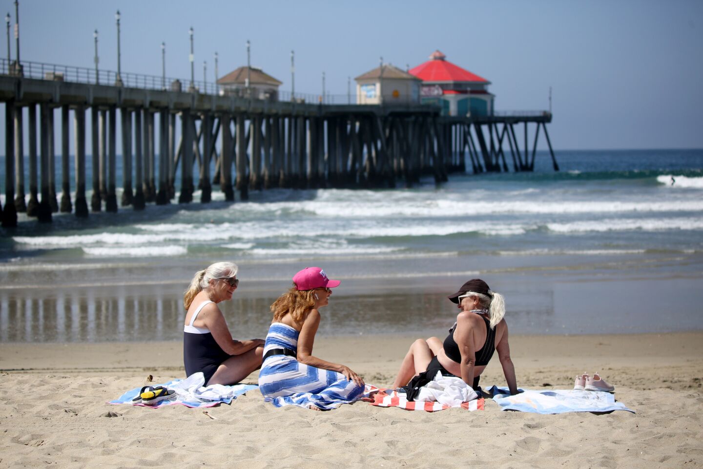 Three women sit on an almost-empty stretch of Huntington City Beach in Huntington Beach on Friday.