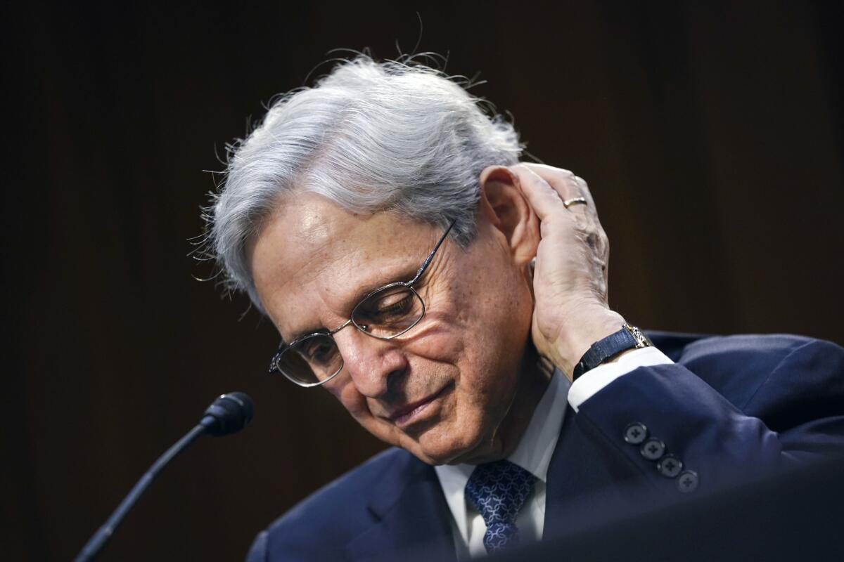 Merrick Garland at a hearing mic looks down, with one hand behind his ear 