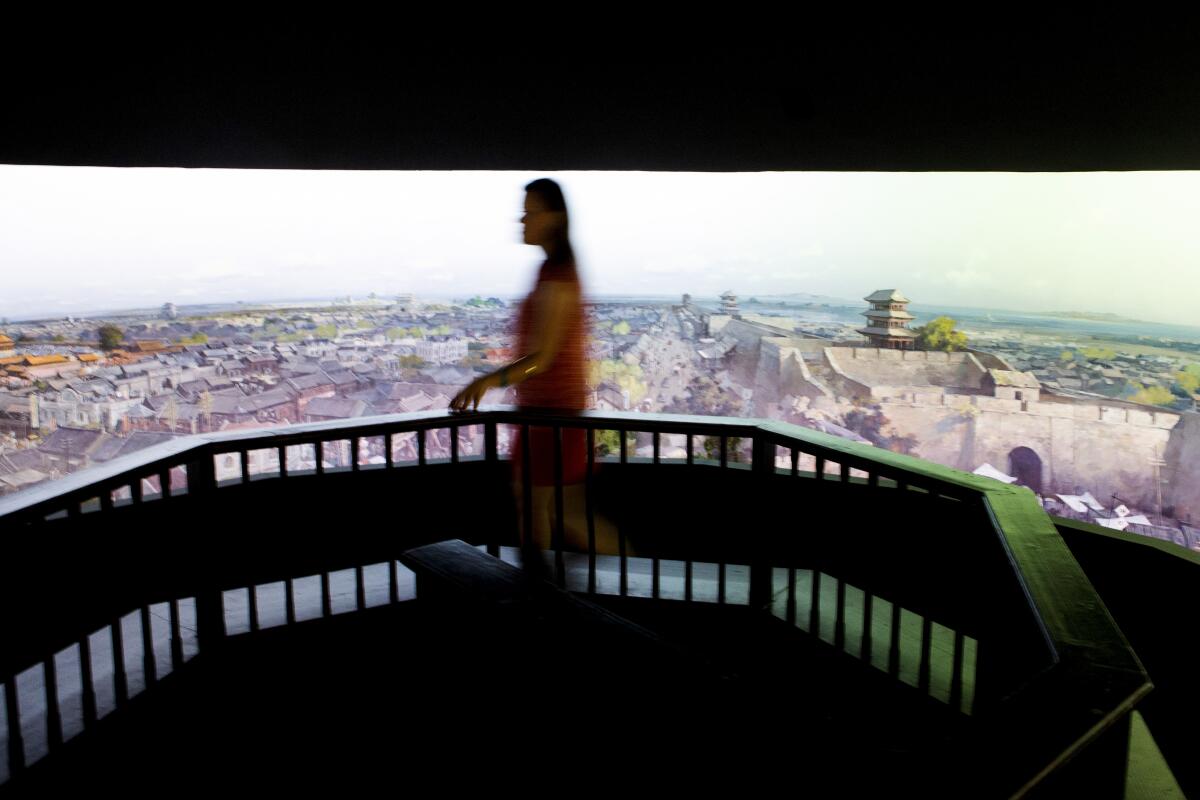 A blurry figure of a woman walks before a 360-degree painting of a Chinese landscape. 