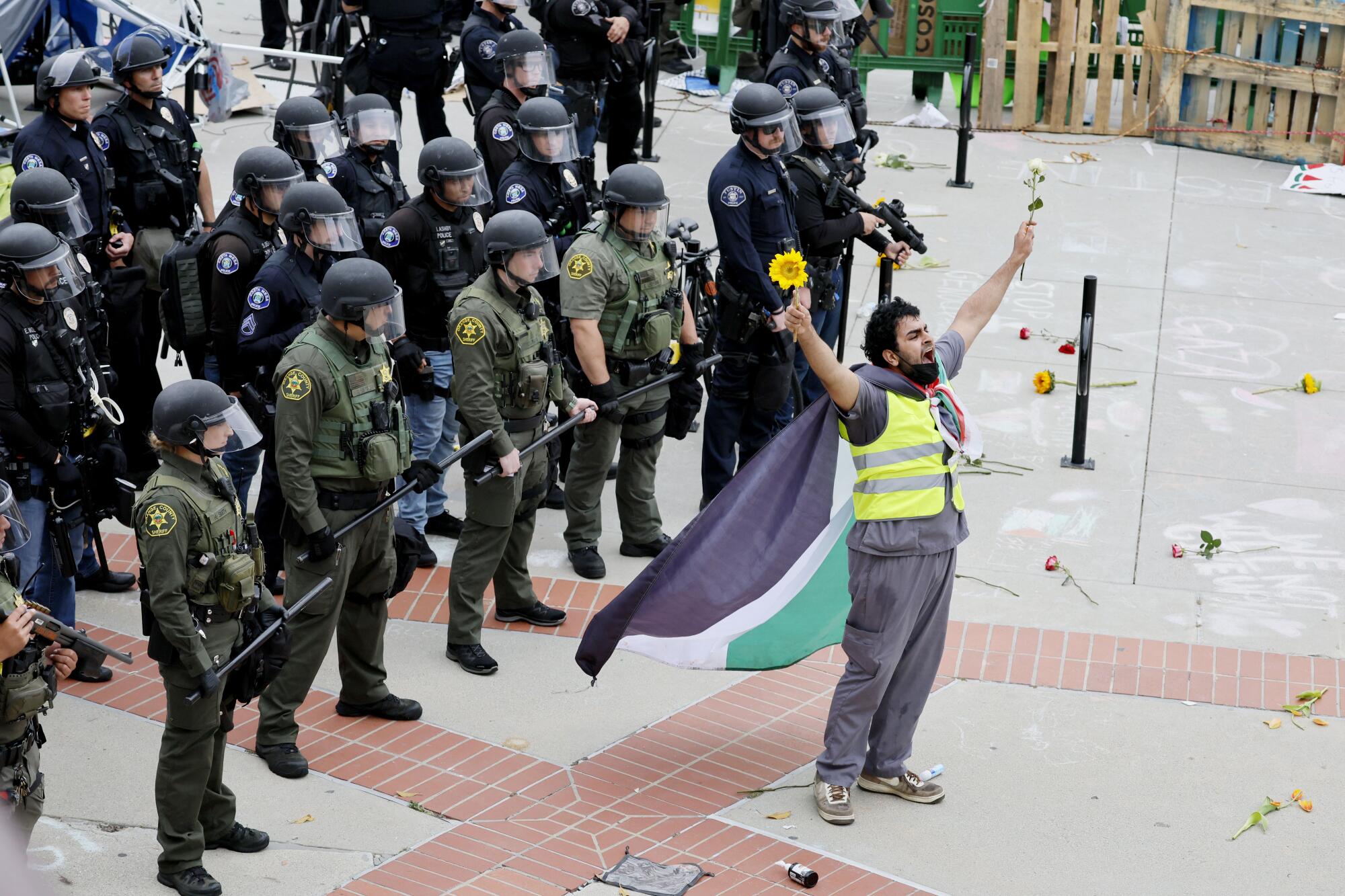 A pro-Palestinian protester stands in front of a line of law enforcement officers from multiple agencies.