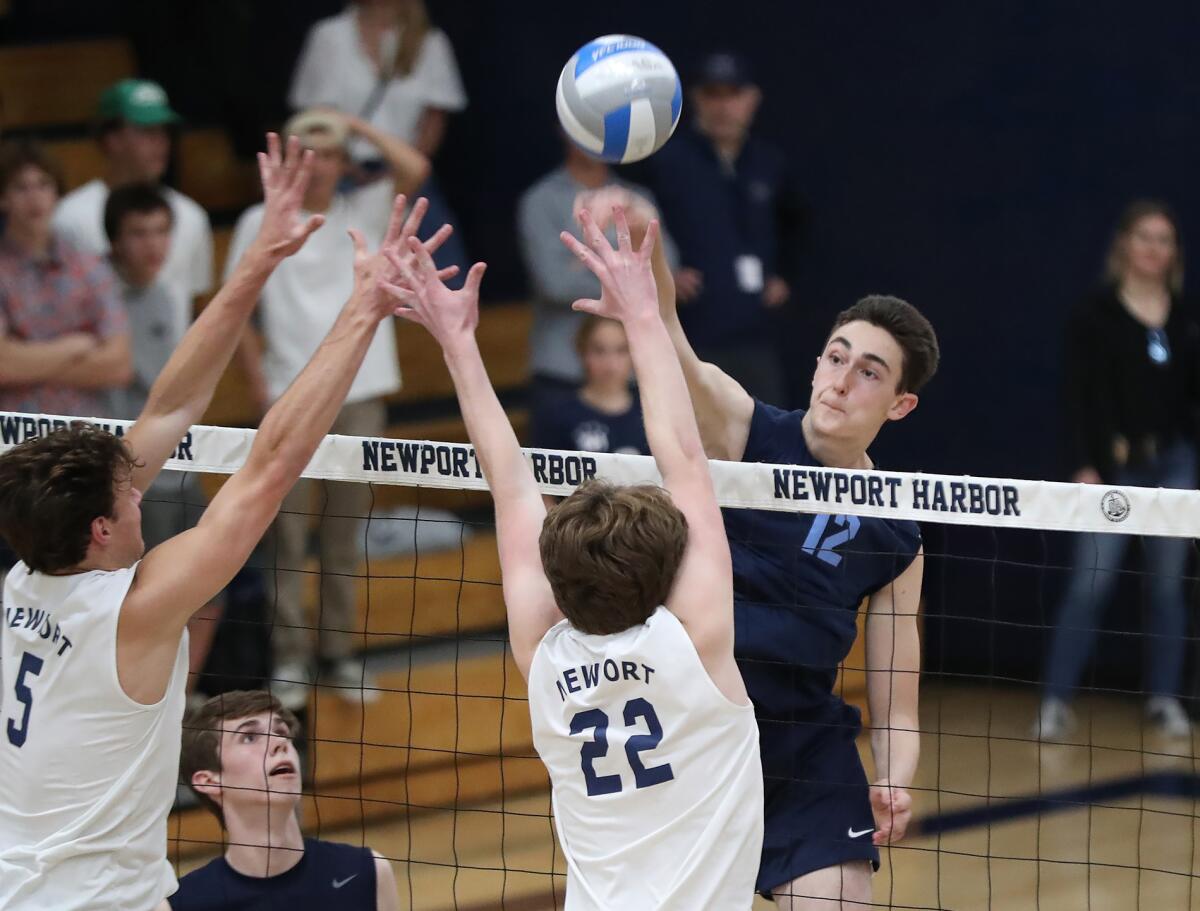 Daniel Booker (12) of Corona del Mar tips a ball past Newport Harbor blockers Riggs Guy (5) and Charlie Herrington (22).