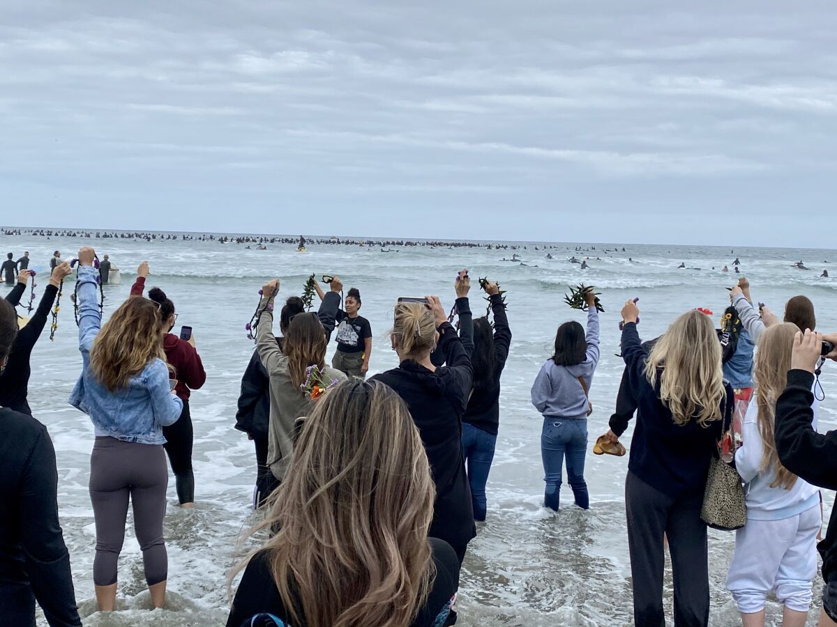 As surfers drop flowers in the waves, other protesters remain on the beach to do the same during the Paddle for Peace.
