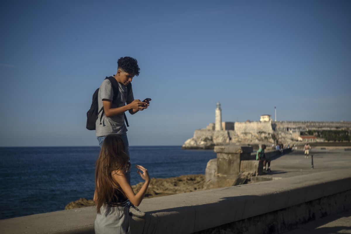A youth uses his smartphone as he and a friend walk along the Malecon seawall in Havana, Cuba, Friday, Nov. 25, 2022. Ever-widening access to the internet is offering a new opportunity for Cubans looking for hard-to-obtain basic goods: online shopping. (AP Photo/Ramon Espinosa)
