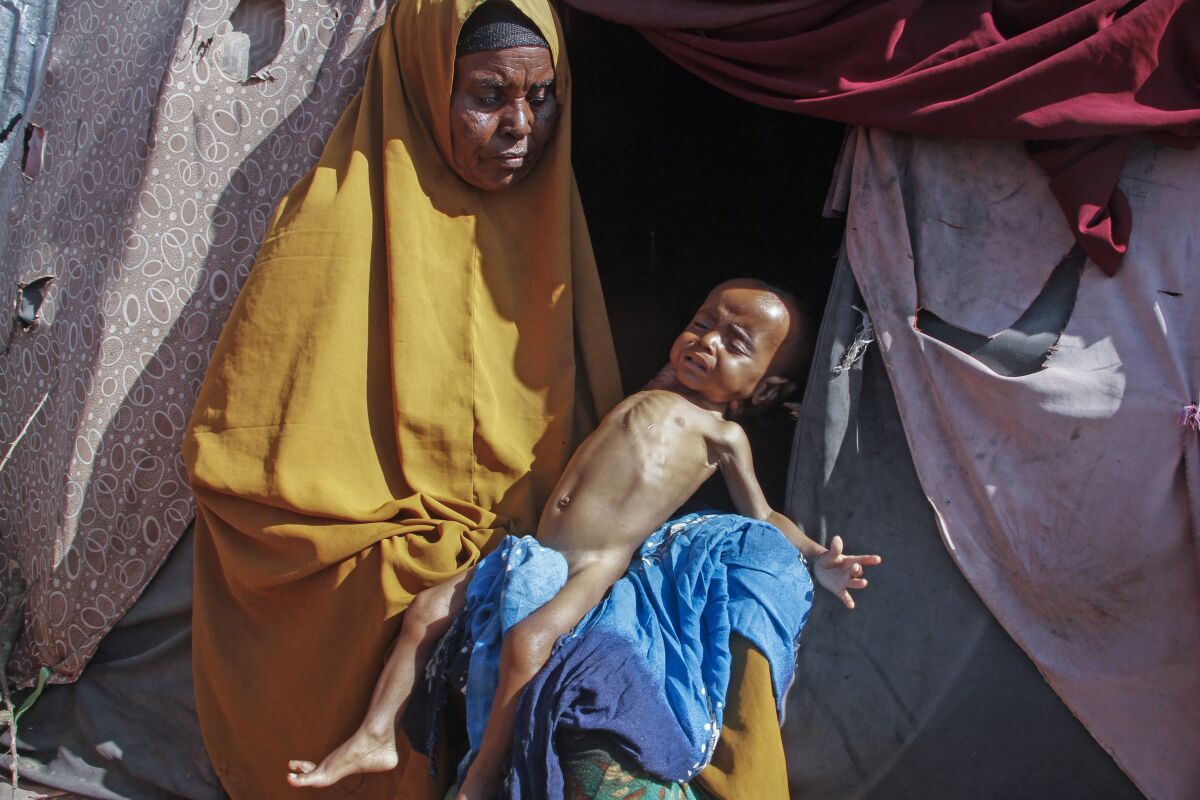 Boolo Aadan, 63, who fled drought-stricken areas, holds her 9 month old grandchild outside the tent where they now live at a makeshift camp on the outskirts of the capital Mogadishu, Somalia Friday, Feb. 4, 2022. Thousands of desperate families have fled a severe drought across large parts of Somalia, seeking food and water in camps for displaced people outside the capital. (AP Photo/Farah Abdi Warsameh)
