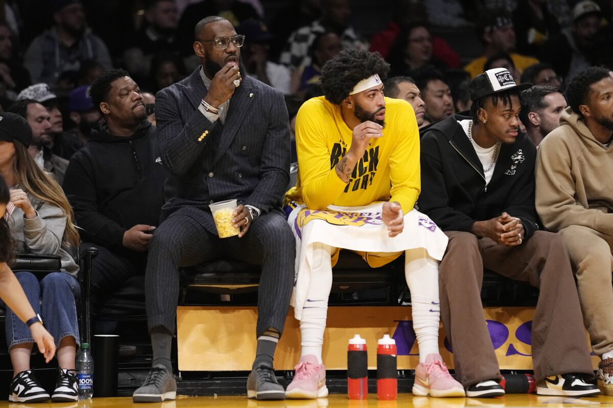 Lakers' LeBron James eats popcorn as he sits next to forward Anthony Davis.