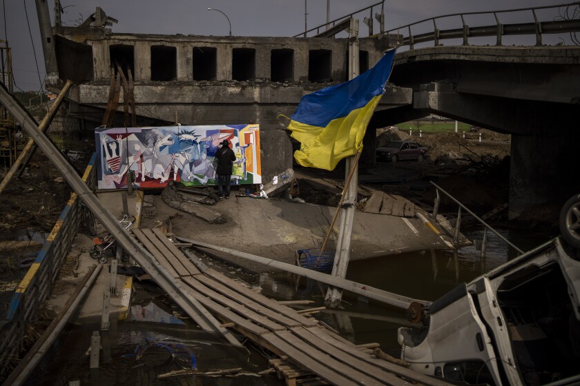A man in black works on a Cubist painting amid a damaged bridge as a blue-and-yellow flag flies nearby