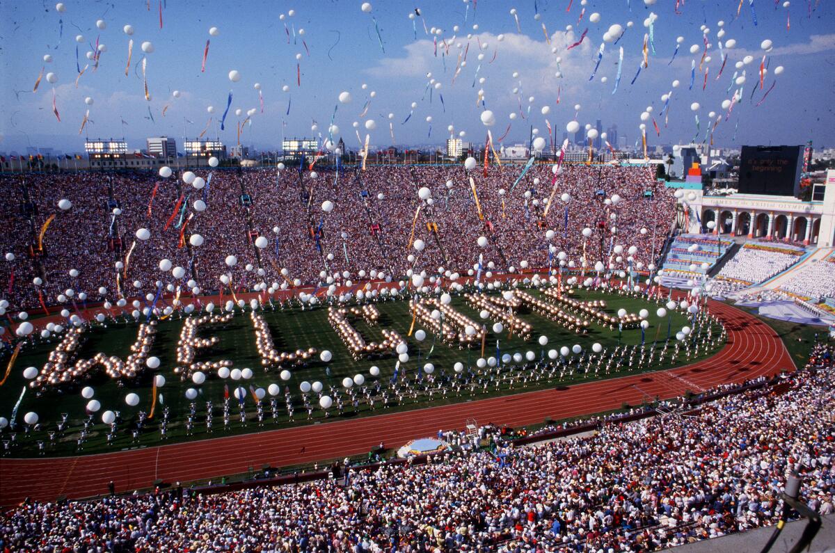 An aerial view of a packed stadium, balloons filling the air and people spelling out the word "welcome" on the field.