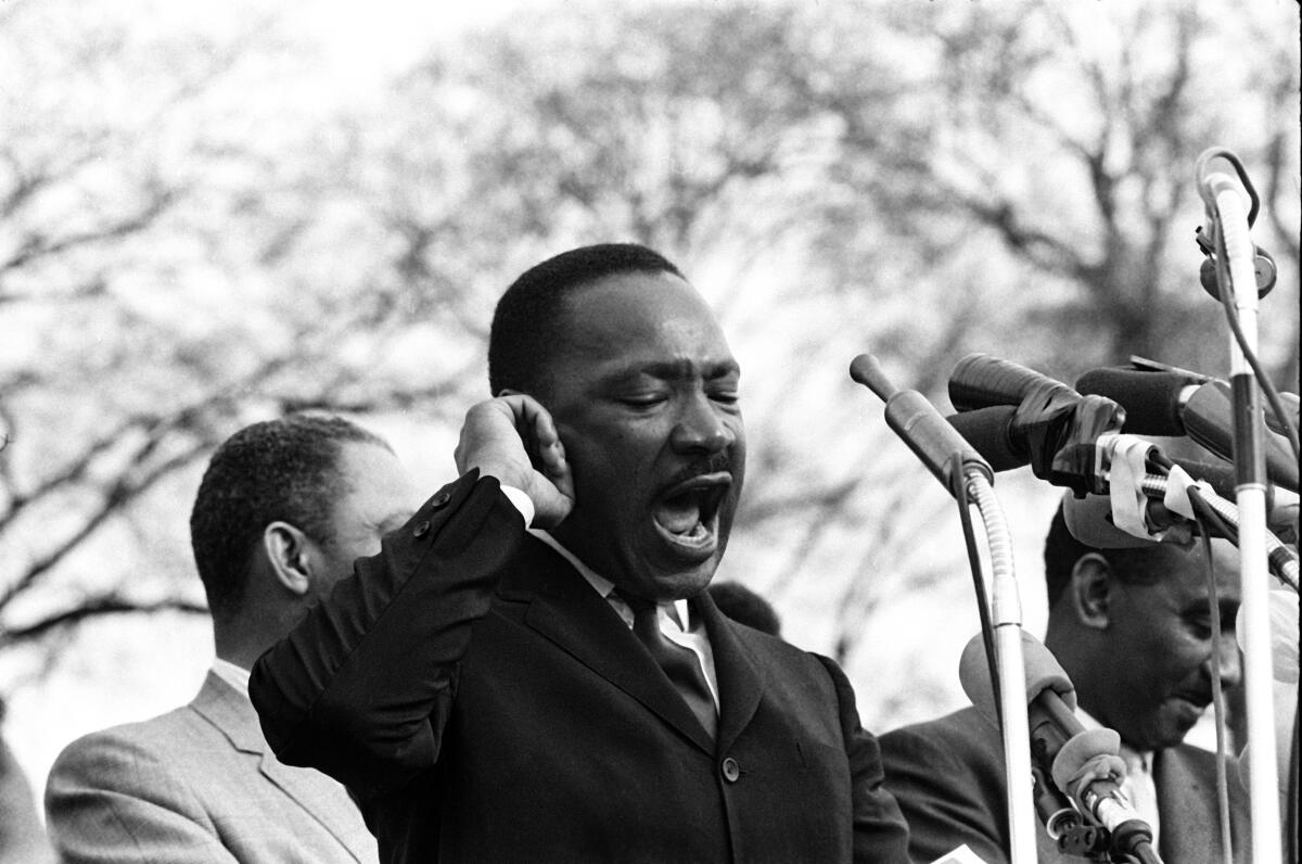 Martin Luther King Jr. speaking into microphones in a black-and-white photo