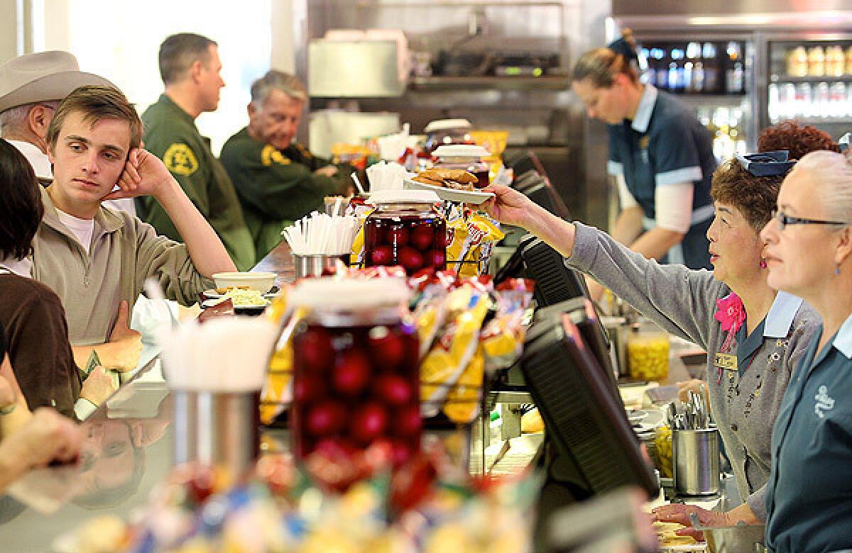 A sandwich is passed across the counter to a customer at Philippe's, which is currently open for takeout or delivery only.