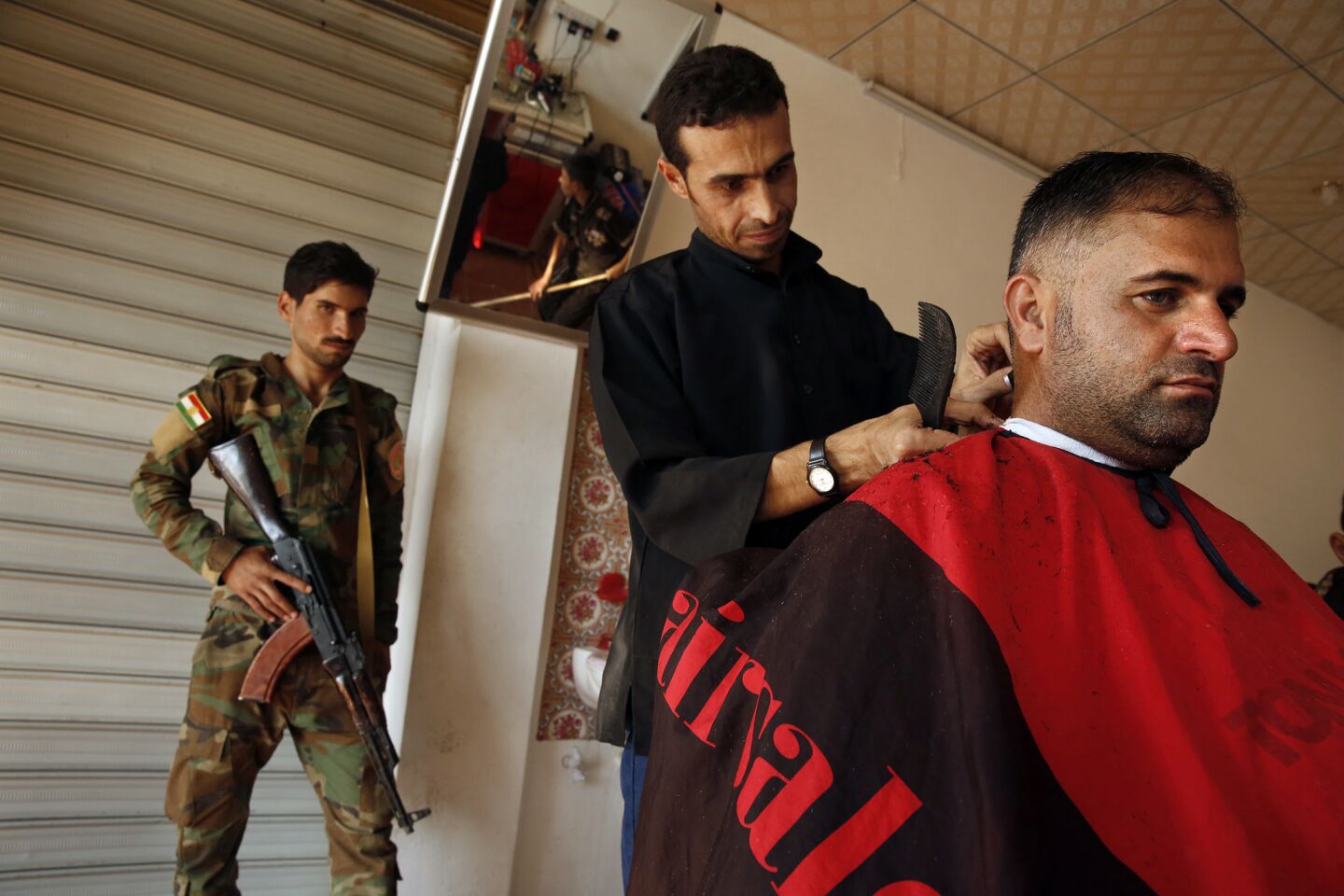 Business is brisk at the barbershops in Faziliya after Kurdish forces retook control from Islamic State militants. A bodyguard stands by.