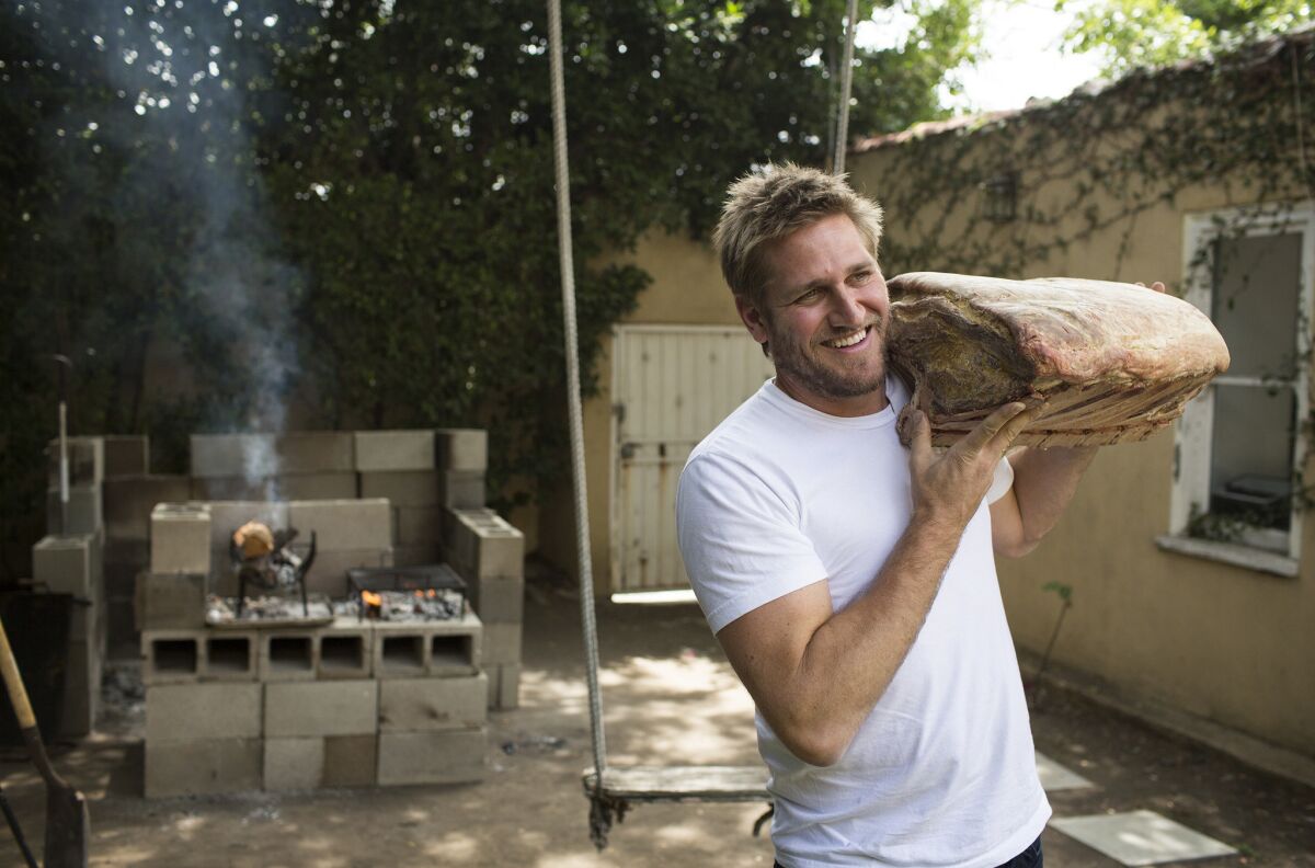 Chef Curtis Stone hefts a piece of meat in the backyard behind his test kitchen in Beverly Hills.