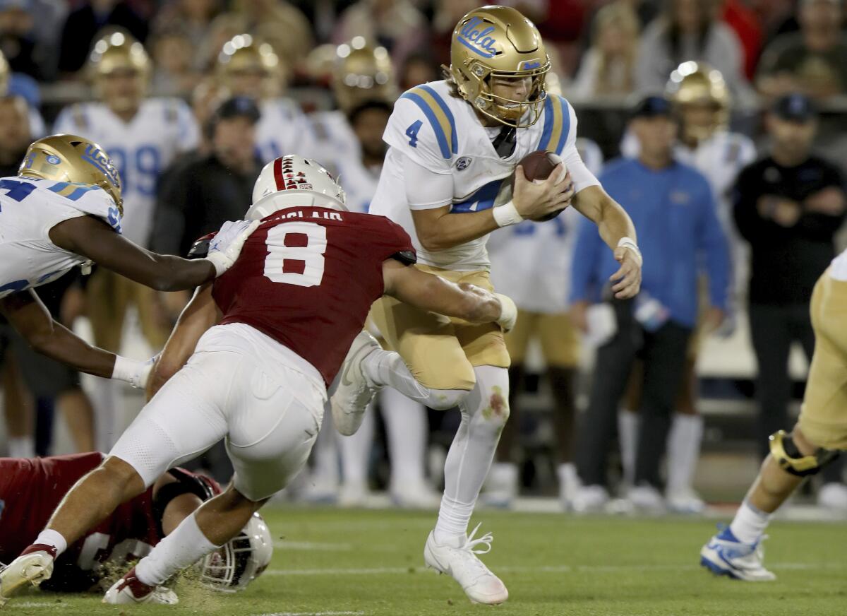 UCLA quarterback Ethan Garbers holds onto the ball and runs as he is hit by Stanford linebacker Tristan Sinclair