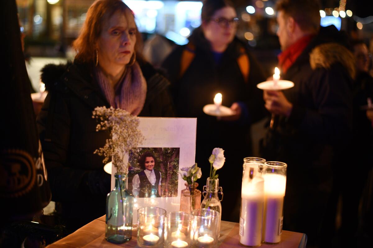 Candles, flowers and a photograph of a teen, with mourners in the background