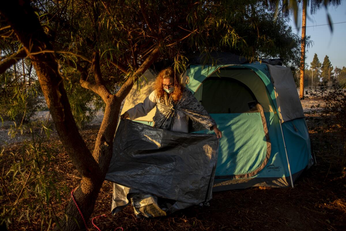A woman folds a tarp outside her tent.