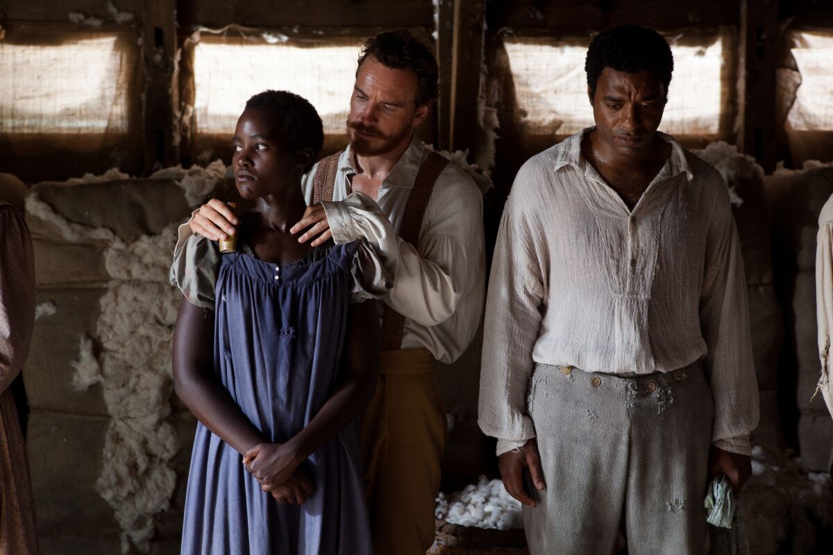 In period costume, a white man puts his hands on a Black woman's shoulders as a Black man stands with eyes downcast.