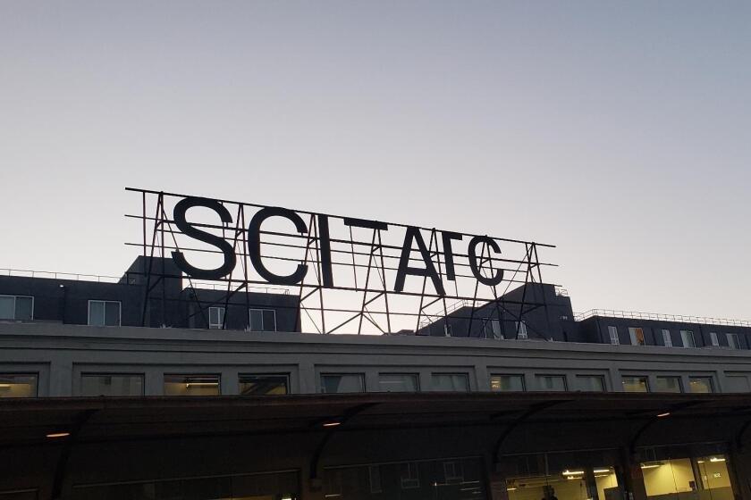 A black metal sign with SCI-Arc's name is silhouetted against a dusky sky