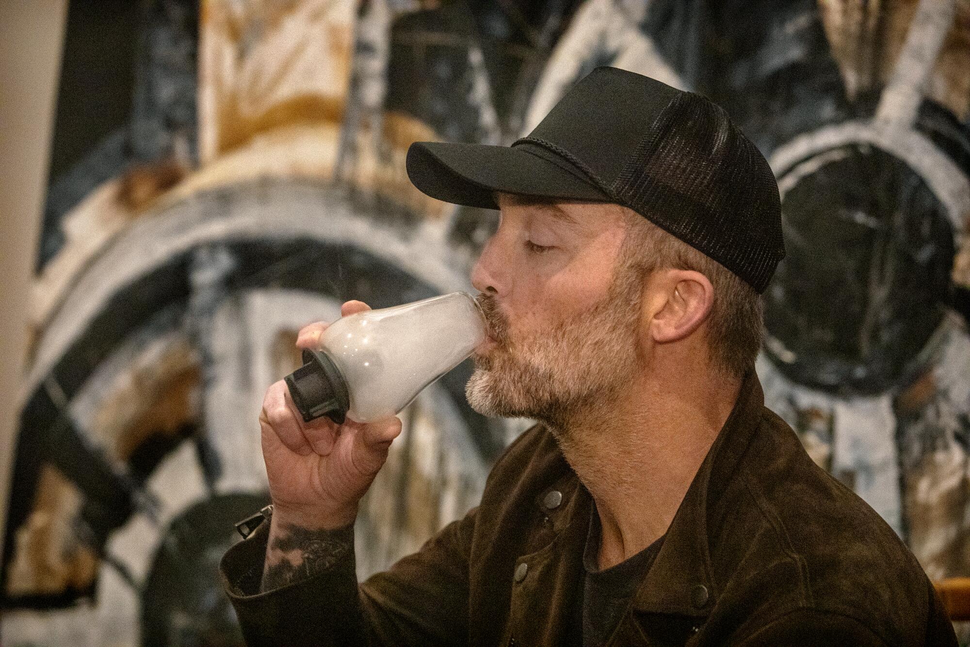 A man in a black ball cap inhales a cup of cannabis vapor